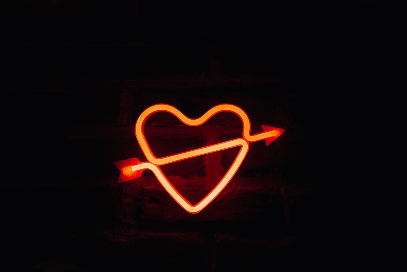 A glowing neon heart with an arrow on a dark background, perfect for romantic themes.